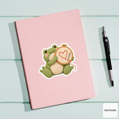 Frog holding up an embroidery hoop with a lopsided heart Vinyl Sticker